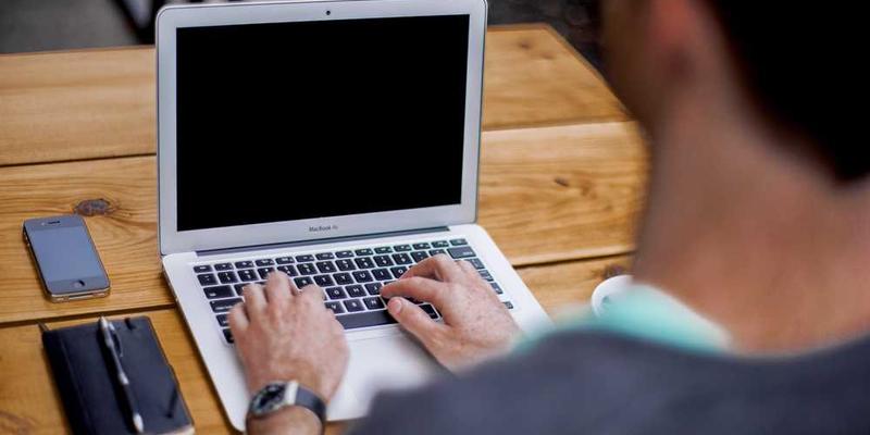 一名学生正在电脑前进行在线学习，旁边放着笔记本，记录下学习心得和笔记。说明：这张图片生动地展现了学生在学习过程中认真思考和记录的学习场景，体现了对知识的渴求和转化的过程.